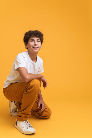 White curly boy wearing suit smiling while crouching isolated over yellow backgroundの写真素材