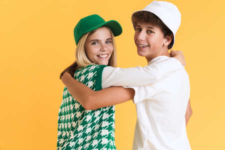 White girl and boy laughing while hugging together isolated over yellow background