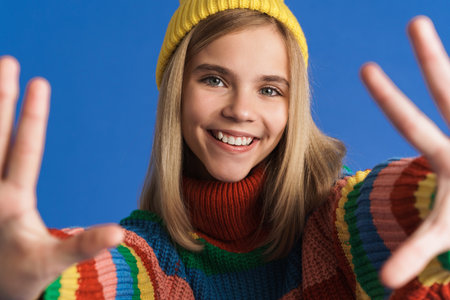 White girl wearing hat smiling and stretching her hands at camera isolated over blue background