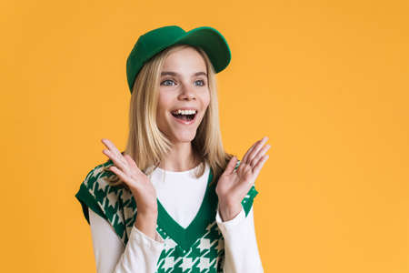 White girl wearing vest smiling and gesturing at camera isolated over yellow backgroundの写真素材