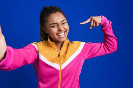 Black young woman pointing finger at herself while taking selfie isolated over blue background