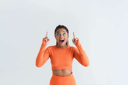 Black excite sportswoman with afro pigtails pointing fingers upward isolated over white backgroundの写真素材