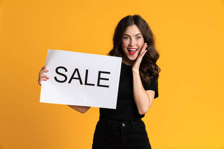White young woman smiling while posing with sale placard isolated over yellow backgroundの写真素材