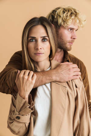 White blonde couple hugging while posing together isolated over beige background