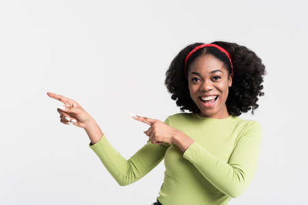 Young black woman smiling and pointing fingers aside isolated over white background