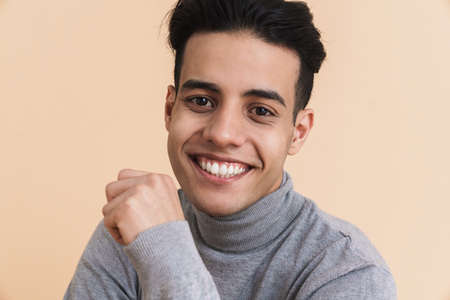 Young middle eastern man smiling and looking at camera isolated over beige backgroundの写真素材