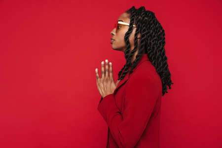 Black young woman wearing jacket looking aside while gesturing isolated over red backgroundの写真素材