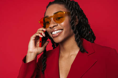 Black young woman smiling while talking on cellphone isolated over red background