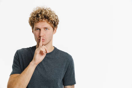 Young man looking at camera while making winner gesture isolated over white wall