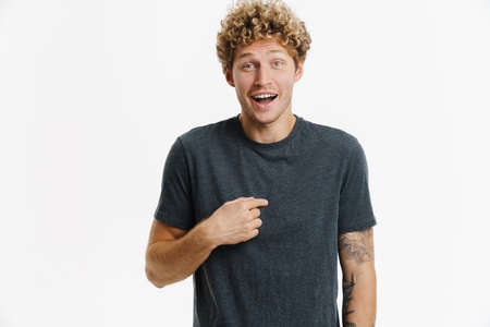 Young excited man laughing while pointing finger at himself isolated over white wall