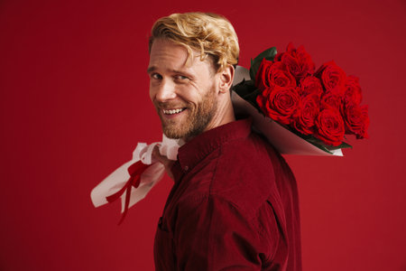 White bearded man smiling while posing with roses isolated over red wallの写真素材