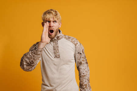 White military man wearing uniform gesturing and screaming isolated over yellow wall