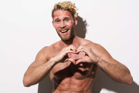 Shirtless blonde man with lipstick smudge showing heart gesture isolated over white backgroundの写真素材