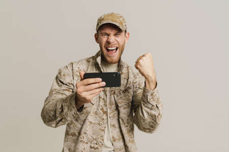 White military man gesturing while playing online game on cellphone isolated over white wallの写真素材
