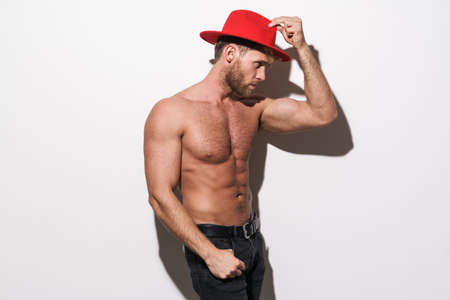 White shirtless man looking aside and posing in red hat isolated over white wallの写真素材