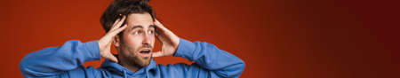 Young man holding his head while expressing surprise isolated over red background
