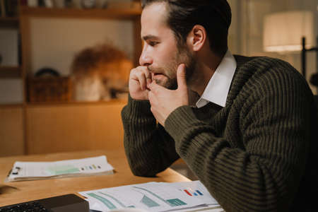 Young bristle man talking on mobile phone while working with laptop in officeの写真素材