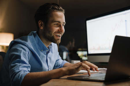Young man working with laptop and computer while sitting at desk in office