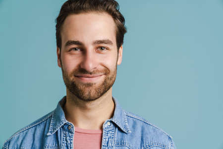 Young bristle man wearing shirt smiling and looking at camera isolated over blue background