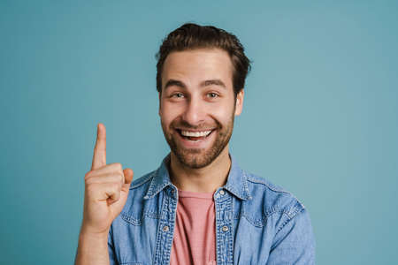 Young bristle man wearing shirt smiling and pointing finger upward isolated over blue background