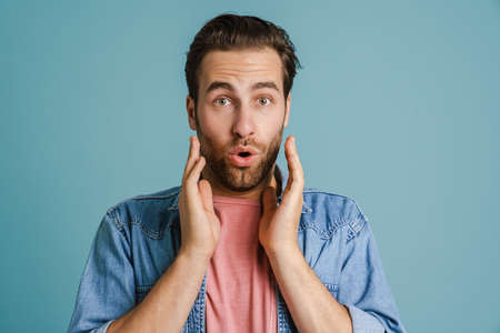 Young bristle man gesturing while expressing surprise isolated over blue backgroundの写真素材