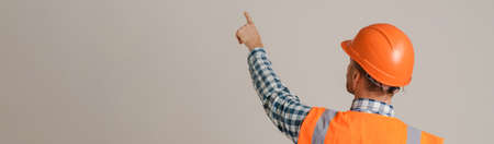 White man worker wearing helmet pointing finger aside isolated over grey background