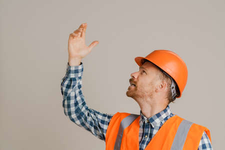 White man worker wearing helmet gesturing and looking upward isolated over grey background