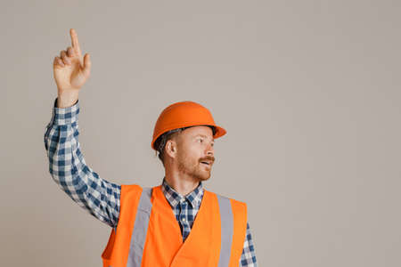 White man worker wearing helmet pointing finger upward isolated over grey background