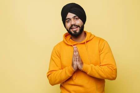 Bearded south asian man making prayer gesture while smiling isolated over yellow wallの写真素材