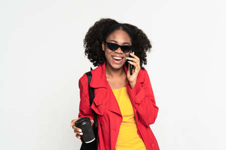 Young black woman talking on cellphone while drinking coffee isolated over white background