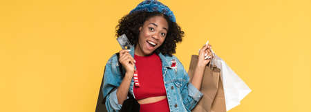 Young black woman posing with credit card and shopping bags isolated over yellow background