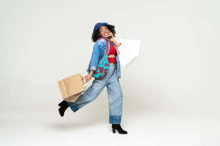 Black woman talking on cellphone while walking with shopping bags isolated over white background