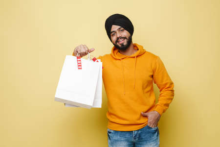 Bearded south asian man wearing turban posing with shopping bags isolated over yellow wallの写真素材