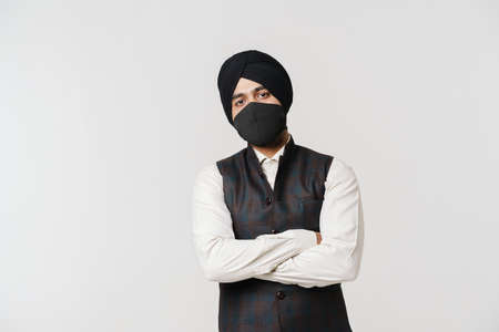 South asian man wearing turban and face mask looking at camera isolated over white wallの写真素材