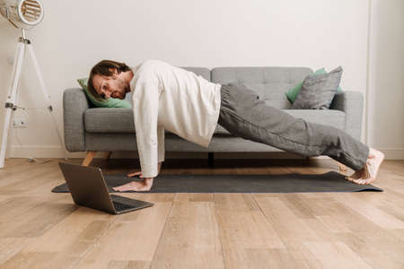 Ginger man using laptop during yoga practice on floor at homeの写真素材