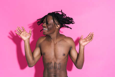 Black shirtless man with dreadlocks making fun on camera isolated over pink backgroundの写真素材