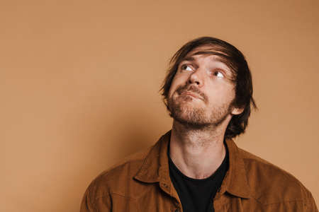 White puzzled man wearing shirt posing while looking aside isolated over beige backgroundの写真素材