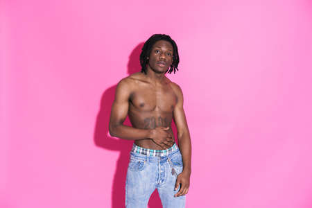 Black shirtless man with dreadlocks posing and looking at camera isolated over pink background