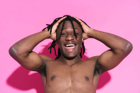 Black shirtless man with dreadlocks laughing while holding his head isolated over pink background