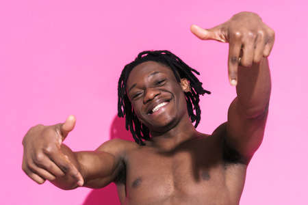 Black shirtless man smiling while pointing fingers downward isolated over pink backgroundの写真素材