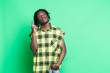 Young black man with dreadlocks looking and pointing finger upward isolated over green backgroundの写真素材