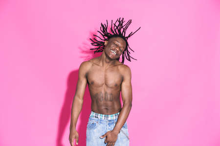 Black shirtless man with dreadlocks laughing and dancing isolated over pink backgroundの写真素材