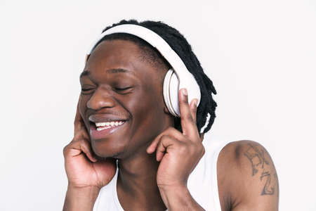 Young black man in headphones smiling while listening music isolated over white backgroundの写真素材