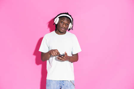Young black man listening music and using mobile phone isolated over pink background