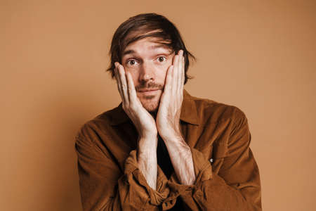White unshaven man holding his face and looking at camera isolated over beige background