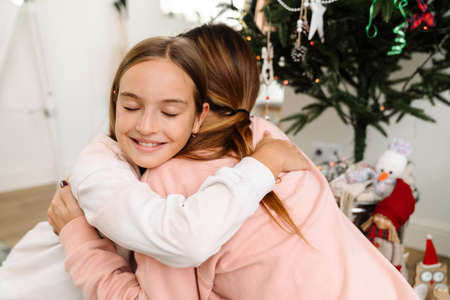 White mother and daughter hugging while decorating christmas tree together at homeの写真素材