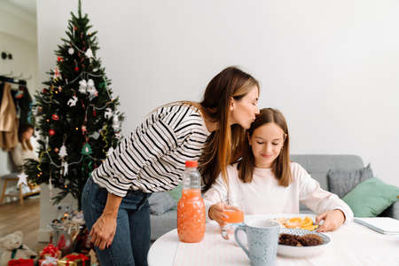 White mother kissing her daughter while having breakfast at homeの写真素材