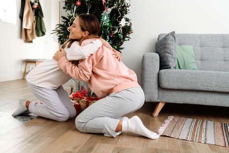 White mother and daughter hugging while decorating christmas tree together at homeの写真素材