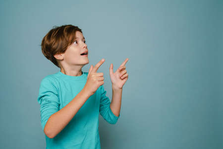 Ginger shocked boy looking and pointing fingers aside isolated over blue wallの写真素材