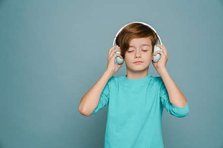 Ginger white boy listening music with headphones isolated over blue wallの写真素材